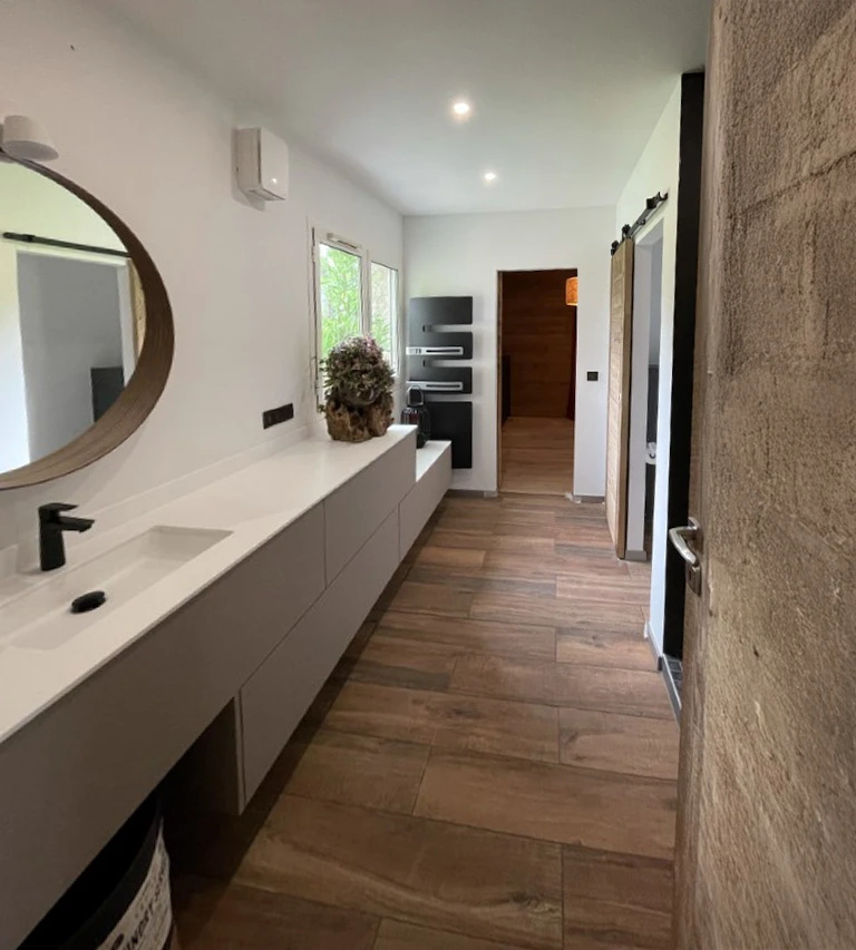 Salle de bain moderne avec meuble vasque suspendu blanc, miroir rond en bois, robinetterie noire mate